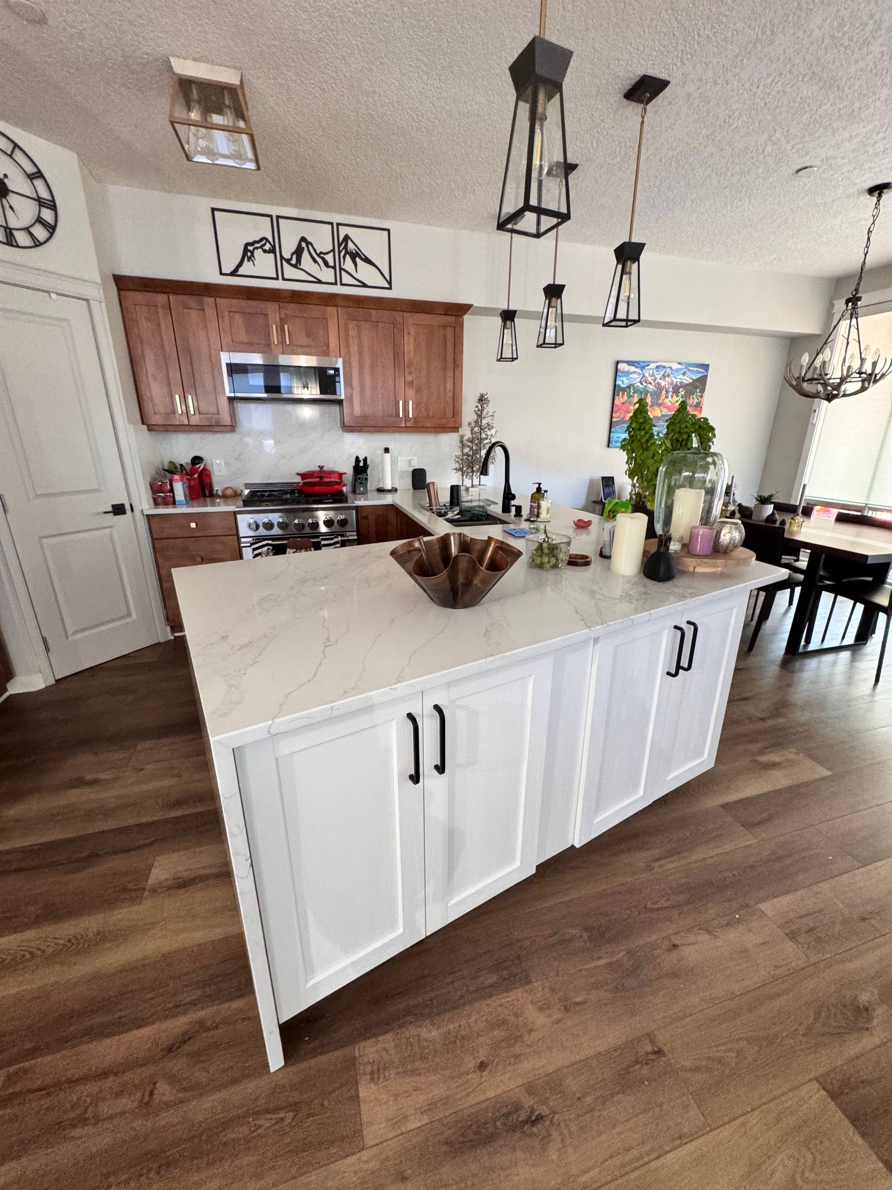 White shaker kitchen island with black pulls and a marble-look top, under black lantern pendants