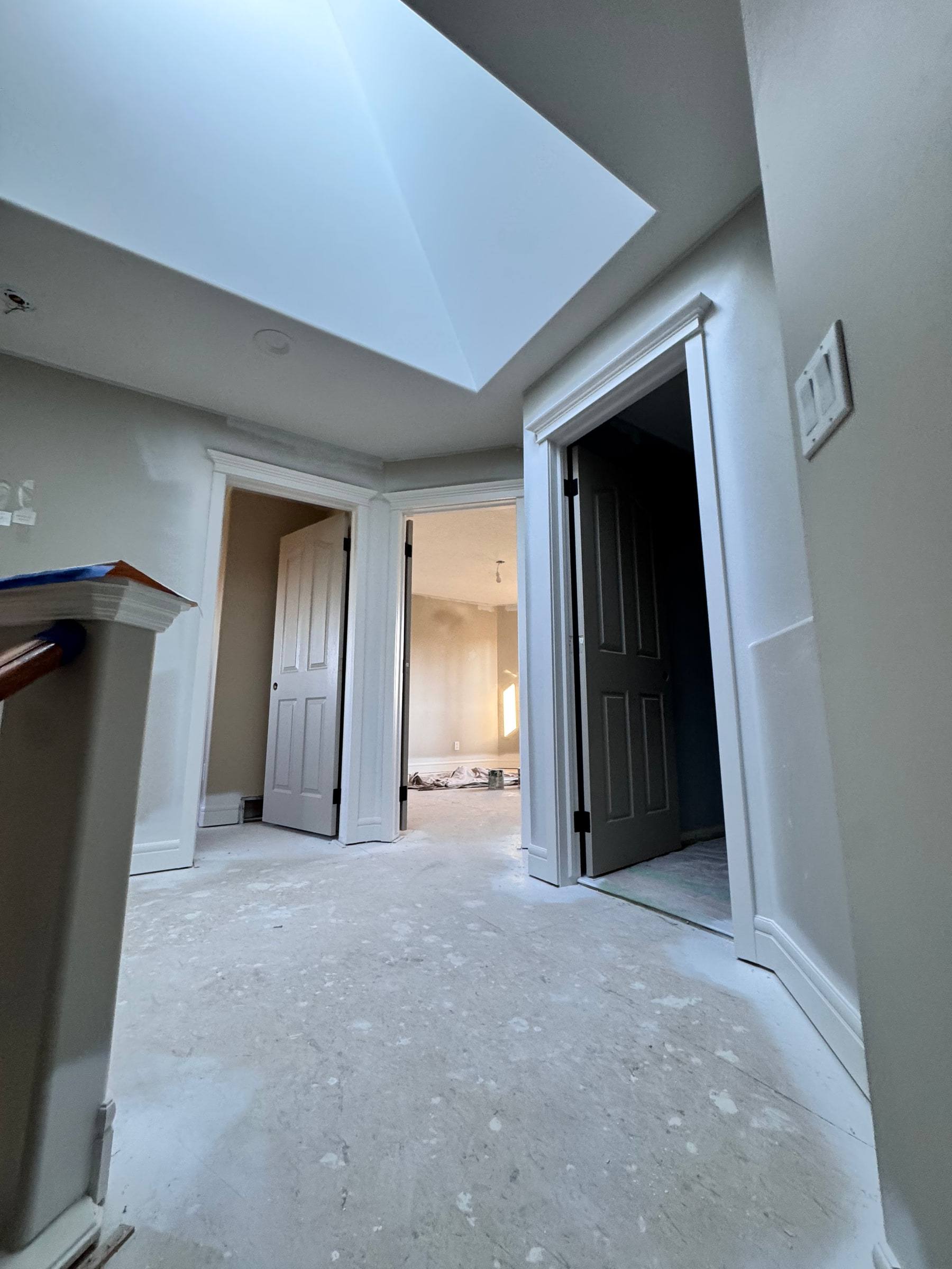 Upstairs hallway under a skylight with new door casings and baseboard on every opening
