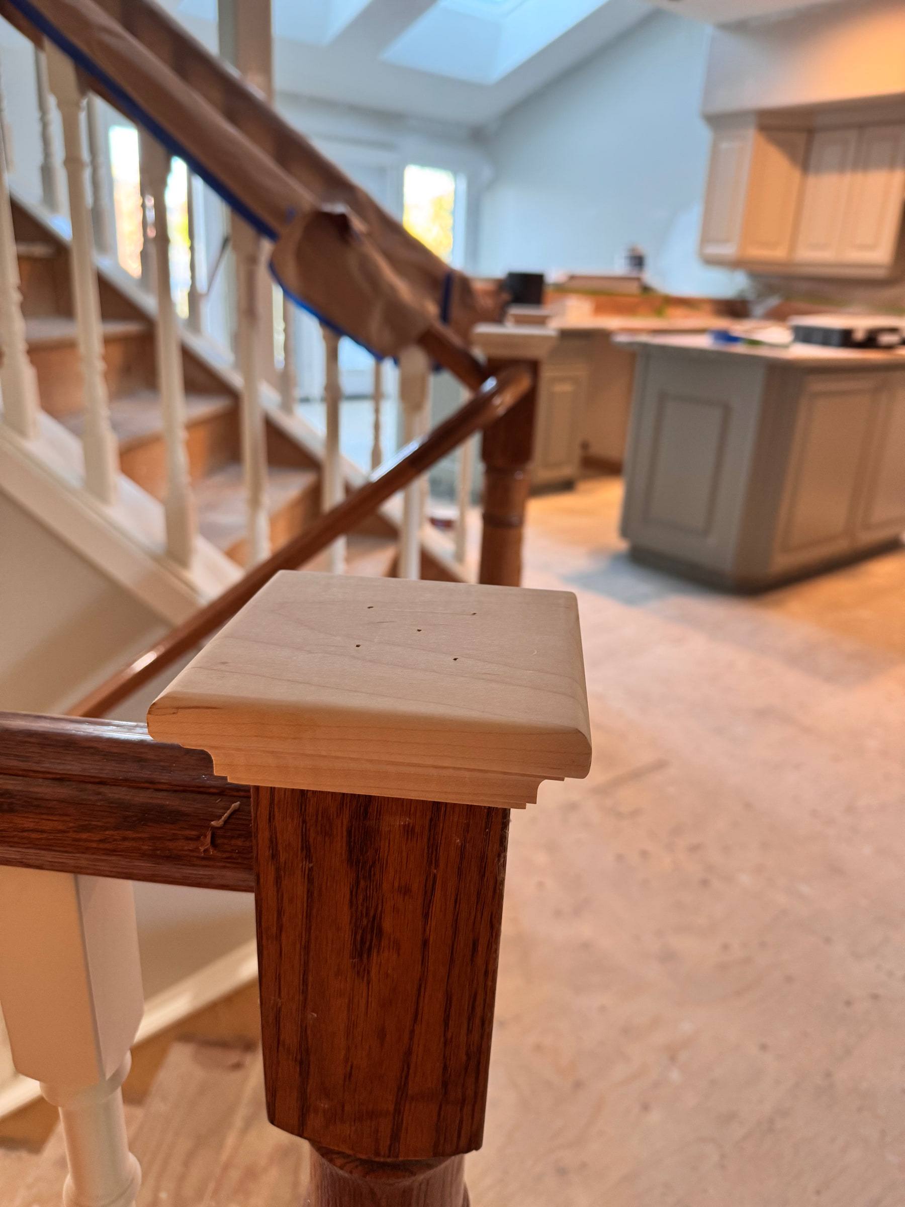 Stained wood newel post with a square cap at the top of a staircase with white spindles