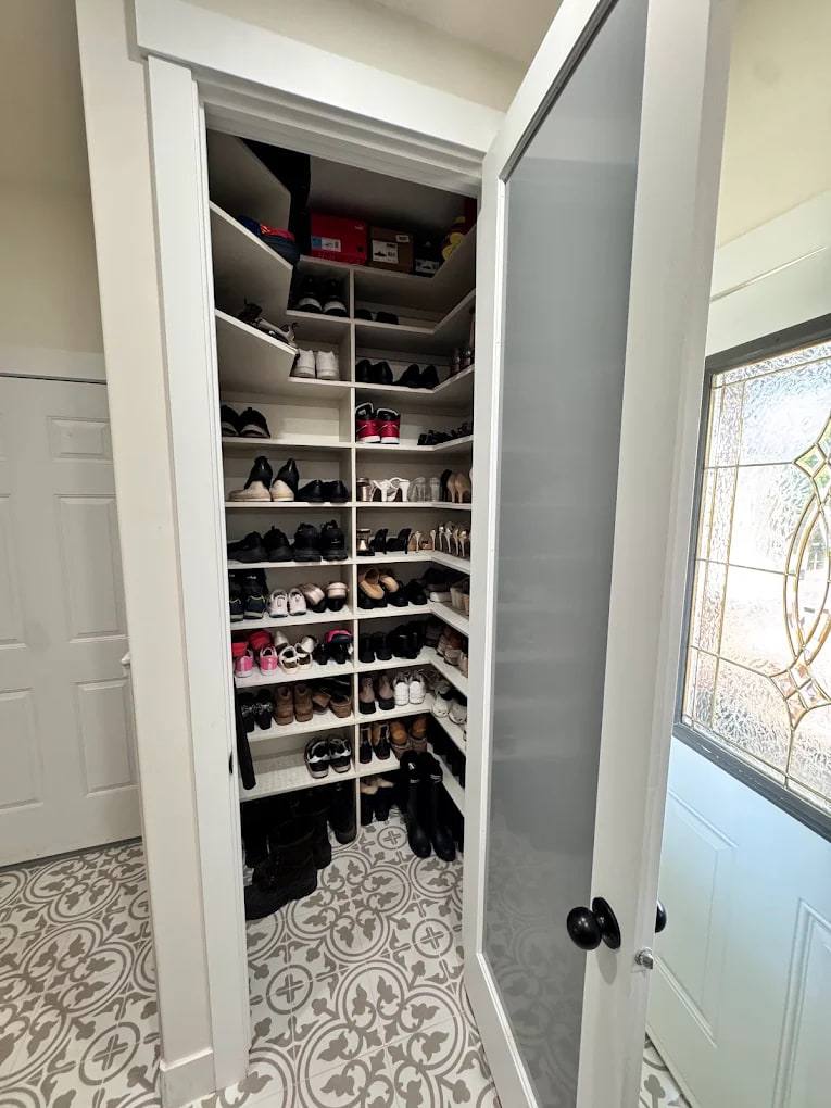 Walk-in shoe closet lined with white adjustable shelves full of shoes