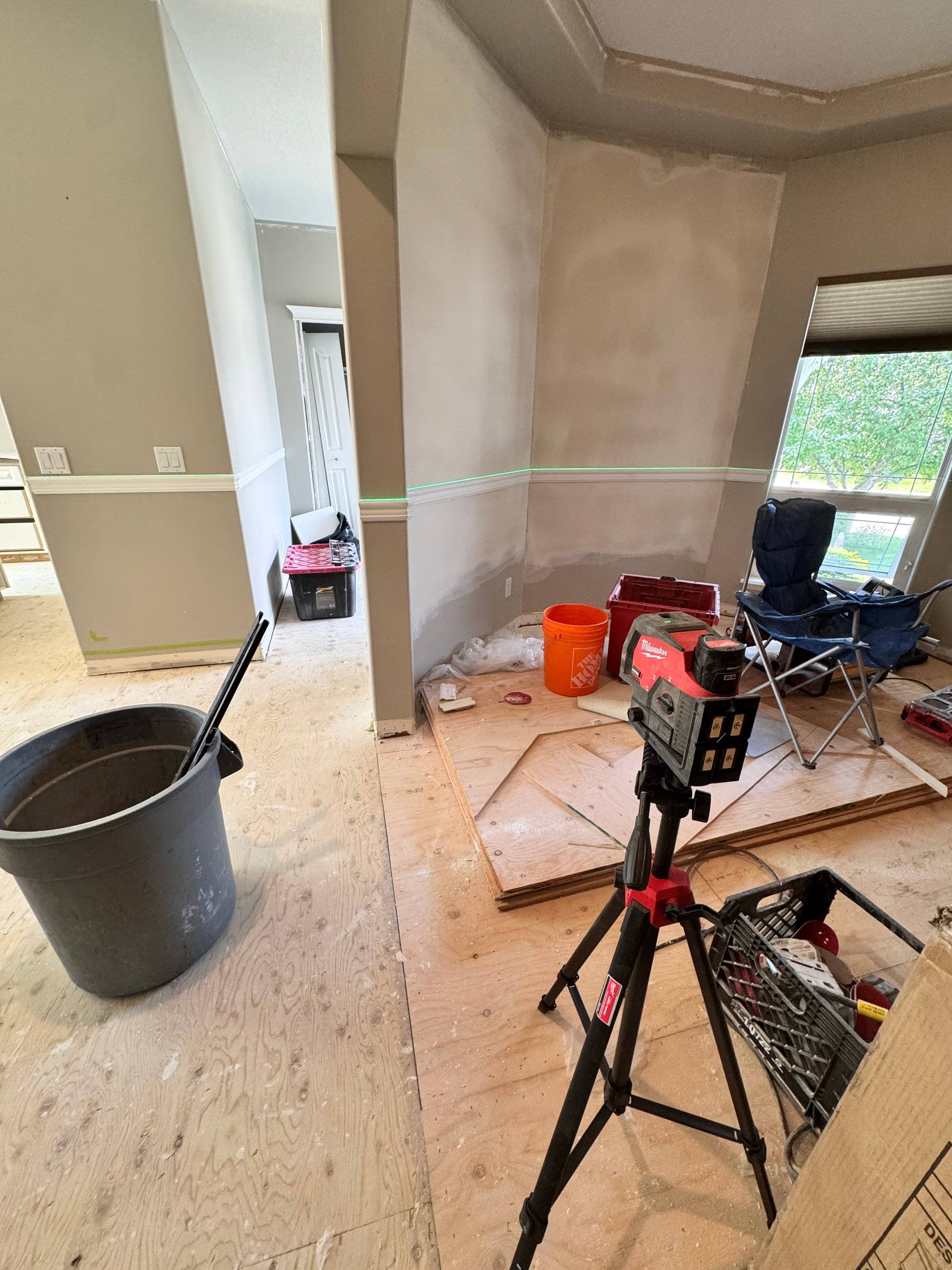 Laser level set up on a tripod to lay out wainscoting heights on a bare subfloor